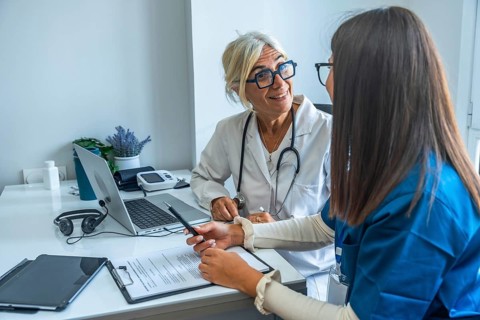 Two medical professionals are discussing important healthcare documents and using a laptop in a