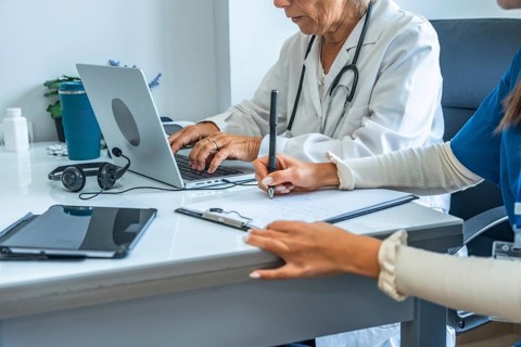 Medical team composed of a doctor and a nurse working together on patient files, with one typing on