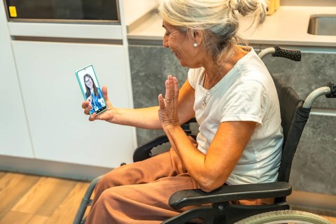 Senior woman in a wheelchair laughing and waving during a video call on her smartphone, connecting