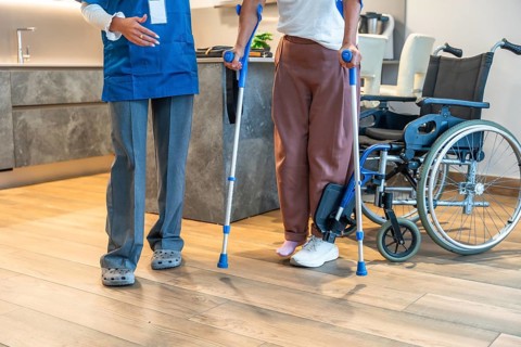 Healthcare professional assisting a patient learning to walk with crutches, providing support