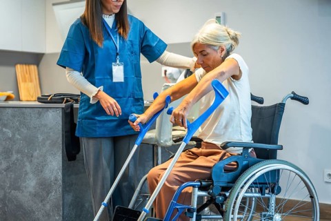 Professional caregiver assisting an elderly woman from a wheelchair, supporting her as she prepares