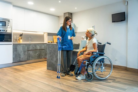 Professional caregiver providing home assistance to a senior woman in a wheelchair, discussing her
