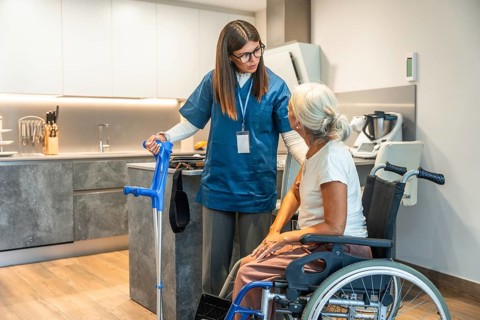 Young female caregiver in scrubs assisting a senior woman in a wheelchair, providing home