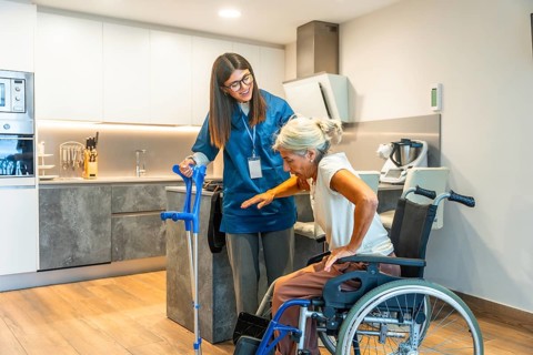Young nurse providing assistance to an elderly woman safely moving from a wheelchair to crutches,