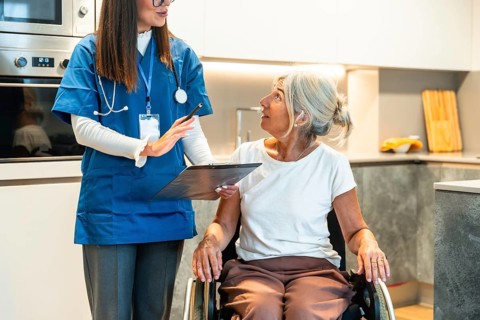 Nurse reviewing a healthcare plan with an elderly woman in a wheelchair in a modern kitchen,