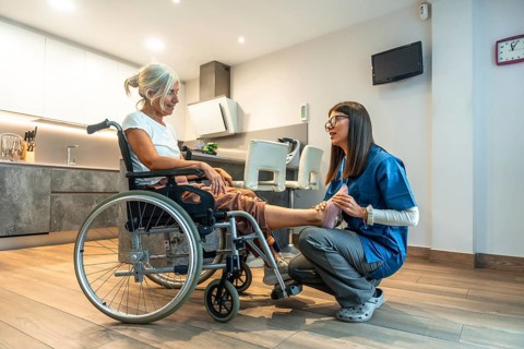 Healthcare professional assisting a senior woman in a wheelchair with foot and leg physical therapy