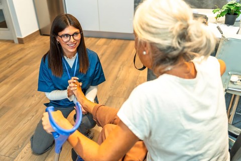 Happy young nurse providing professional foot physical therapy and care to an elderly woman using