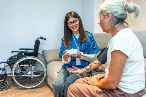 Healthcare professional checking blood pressure for an elderly patient while providing medical