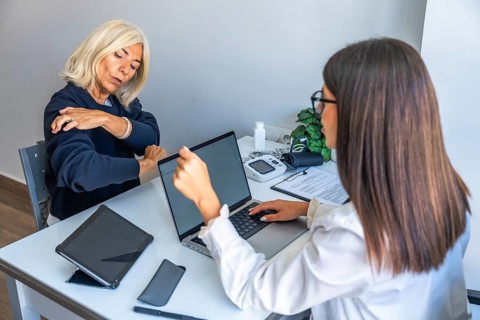 Female doctor consulting with elderly woman about shoulder pain and treatment options, using a