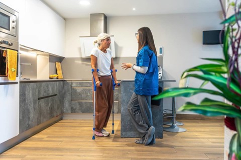 Home caregiver interacting with a senior woman using crutches, providing support and advice for her