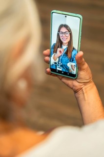Senior woman holding smartphone for a telemedicine video call with doctor, receiving virtual