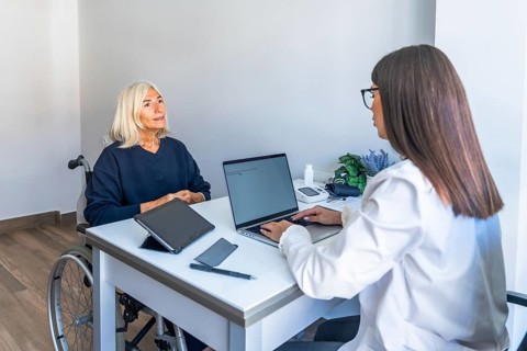 Female doctor consulting with an older woman in a wheelchair, discussing treatment and care while