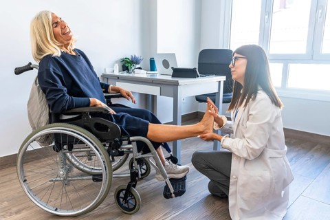 Female doctor examining and rehabilitating a senior woman's leg and ankle, who is seated in a