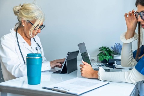Two female medical professionals are collaborating and working together at a desk, utilizing