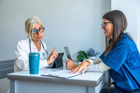 Experienced doctor discussing treatment with a smiling young nurse, both utilizing digital tablets