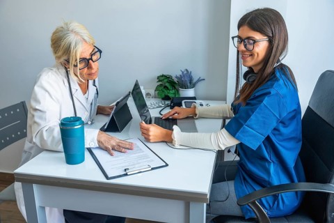Female physician and junior nurse collaborate in a modern clinic office, reviewing patient data on