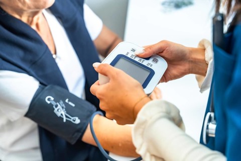 Healthcare professional checking a senior woman's blood pressure at home or in a clinic, focusing