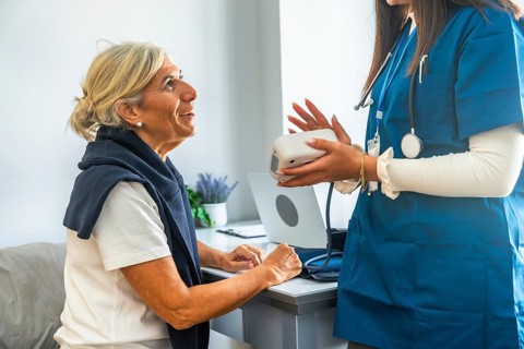 Healthcare professional in blue scrubs holding a blood pressure monitor, explaining its use to an