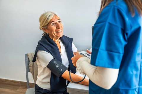 Nurse measuring blood pressure of smiling elderly woman during routine clinic checkup, highlighting