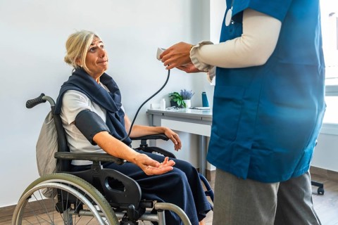 Nurse monitoring blood pressure of an elderly woman using a medical device while she is sitting in