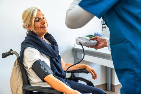 Senior woman in a wheelchair having her blood pressure measured by a medical professional,