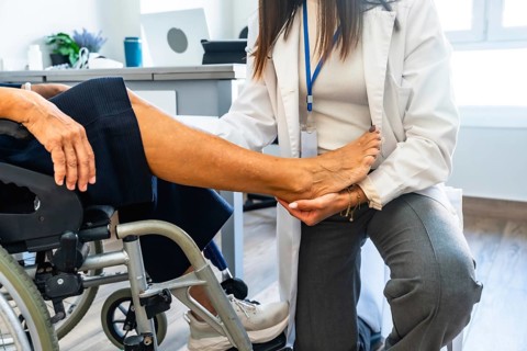 Healthcare professional wearing a lab coat and examining the leg of a senior patient sitting in a