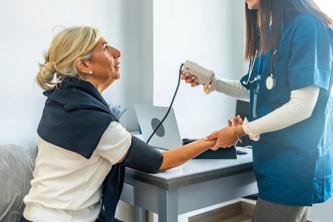 Young medical professional in blue scrubs carefully checking the blood pressure of a smiling senior