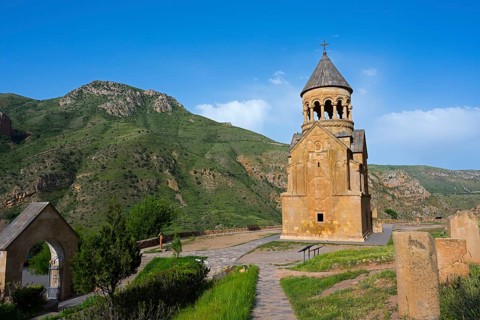 A chapel against a green mountain landscape under a blue sky, surrounded by nature, Noravank