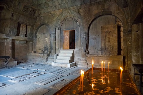 Ancient stone room with candles and grave plaques creating a calm and mystical atmosphere, Noravank