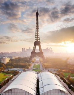 The Eiffel Tower is a tall structure in the background of a city. The sky is cloudy and the sun is