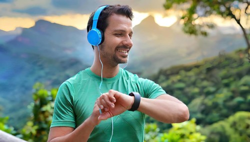 A man wearing headphones and a green shirt is smiling and looking at his watch. He is wearing a