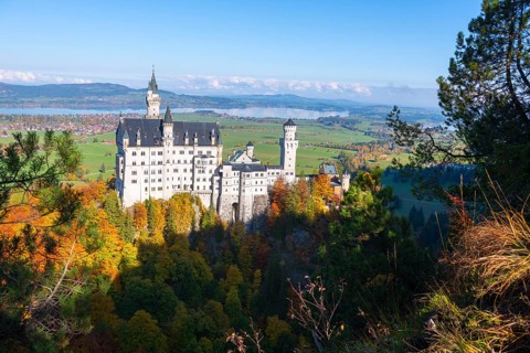Fairytale Neuschwanstein Castle surrounded by autumnal forest and blue sky in picturesque