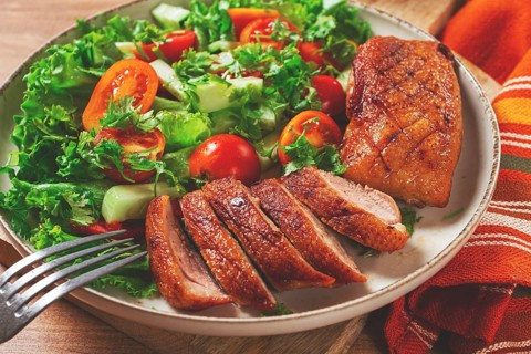 Delicious grilled duck breast served with fresh garden salad and cherry tomatoes at a rustic dining