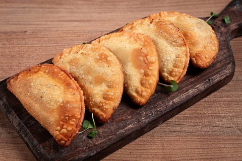 Fried chebureks, deep-fried, mini, on a chopping board, wooden table, close-up, no people