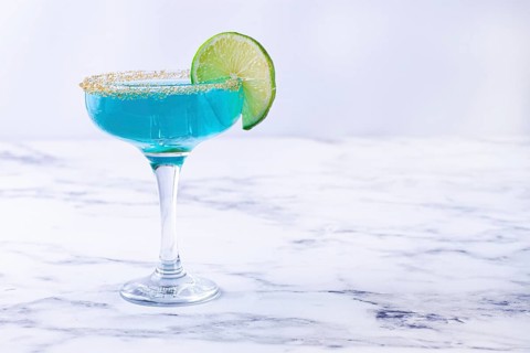 Bright blue cocktail with a slice of lime on a marble surface