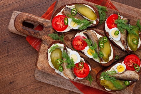Sandwiches on rye bread with sprats, quail eggs, fresh tomatoes and pickled cucumber, on a wooden