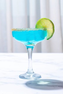 Bright blue cocktail with a slice of lime on a marble surface