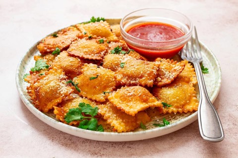 Fried ravioli with parmesan cheese, served with red sauce and garnished with herbs, on a light