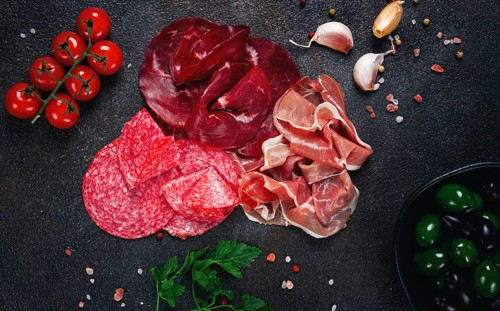 Assorted dried meat, fresh tomatoes and olives spread out on a dark surface, food composition, top