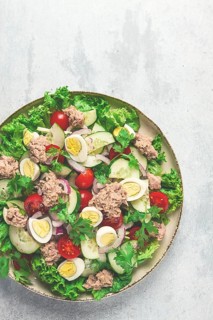 Tuna salad, vegetable salad with quail eggs, lettuce, red onion and cucumbers, on a light gray