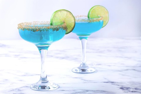 Colorful blue cocktails in elegant glasses with lime garnish on a marble table