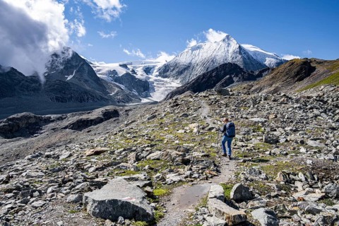 Hiker on rocky path with impressive views of snow-covered mountain landscape, Mont Blanc de Cheilon