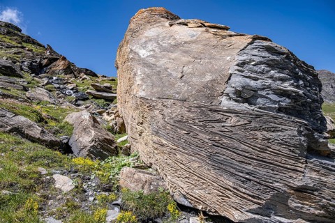 Large rock in the foreground shows fascinating rock structures under a blue sky, Valais Alps,
