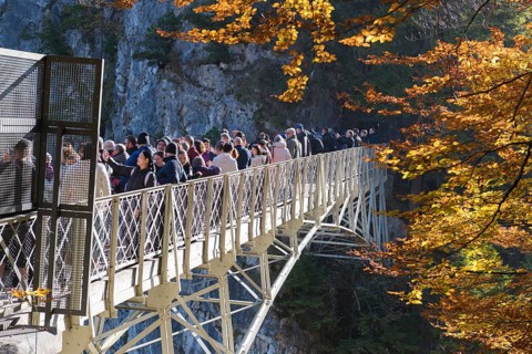 Group of people on Marienbrücke near Neuschwanstein, surrounded by autumn trees and rocks,