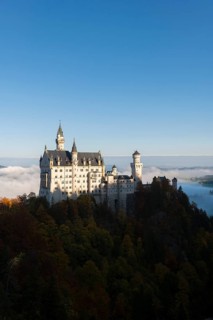 Neuschwanstein Castle towers over a sea of clouds and forests in the autumn sun, Schwangau near