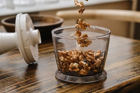 A person is preparing to chop walnuts using a food processor in a cozy kitchen. The walnuts are
