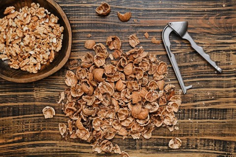 Walnuts are being shelled on a rustic wooden surface. A bowl of walnut pieces sits nearby, while