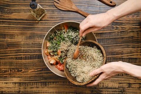 Adding ground walnuts to a bowl with chopped vegetables and herbs. A wooden spoon is used to