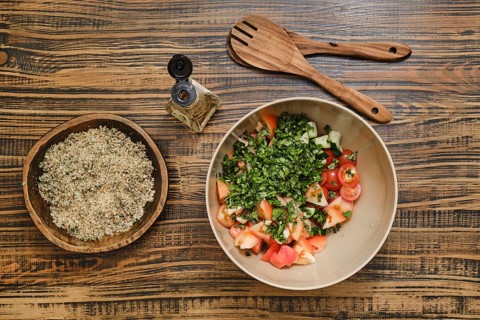 Chopped tomatoes and fresh herbs in a bowl ready for mixing. A bowl with crushed walnuts is nearby,
