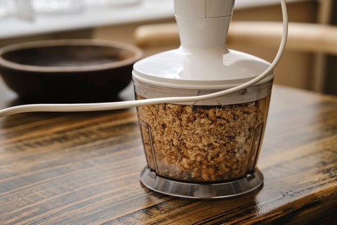 Chopping walnuts in a food processor on a rustic wooden table. The device is plugged in and the